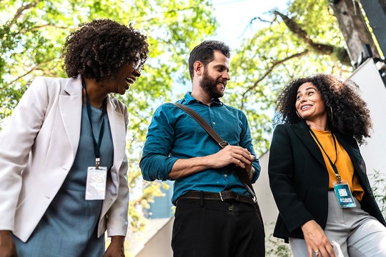 Three professionals with curly hair are engaged in a friendly conversation outdoors. They are surrounded by greenery, creating a vibrant and cheerful atmosphere.