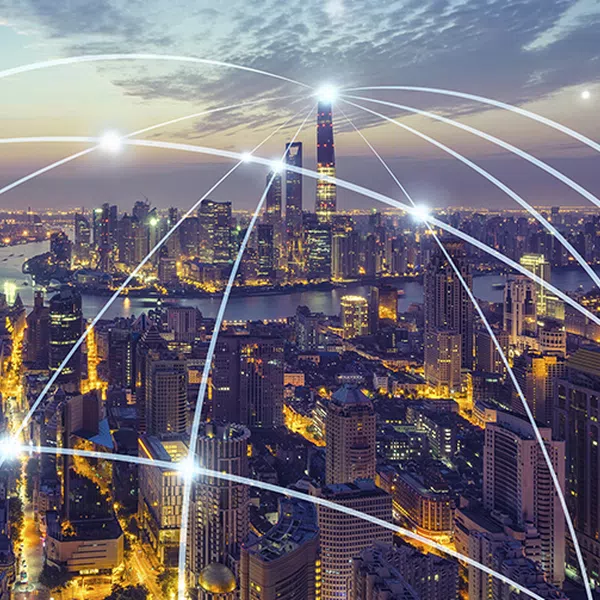A city skyline at dusk features bright buildings and illuminated streets, while glowing lines connect various points, suggesting a network or digital communication across the urban landscape.